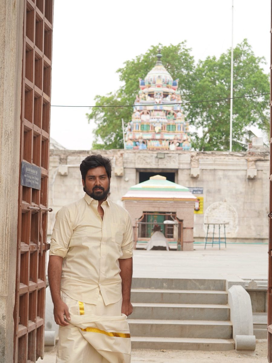 Avinash Srinivasan, the author of this article, standing at the entrance of a Tamil temple in a veshti and shirt.